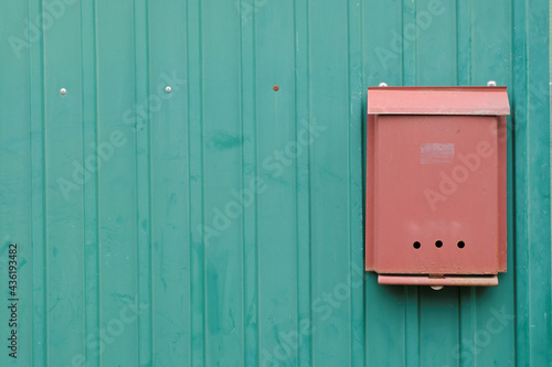 An orange metal mailbox on the iron green fence of a country house.