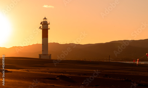 Sunset picture captured in  Fangar  Beach with a beautiful lighthouse and the sun hiding it behind the mountains. Ebro Delta  Tarragona  Spain.