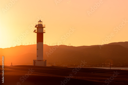Sunset picture captured in "Fangar" Beach with a beautiful lighthouse and the sun hiding it behind the mountains. Ebro Delta, Tarragona, Spain.