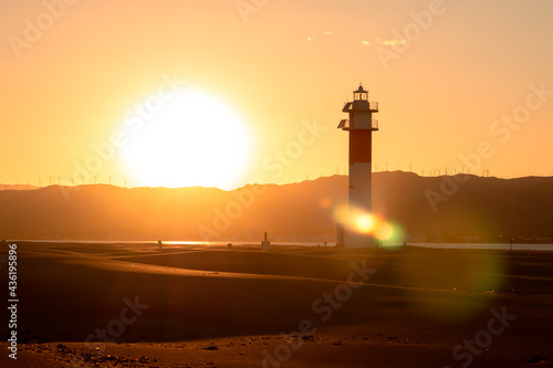 Sunset picture captured in "Fangar" Beach with a beautiful lighthouse and the sun hiding it behind the mountains. Ebro Delta, Tarragona, Spain.