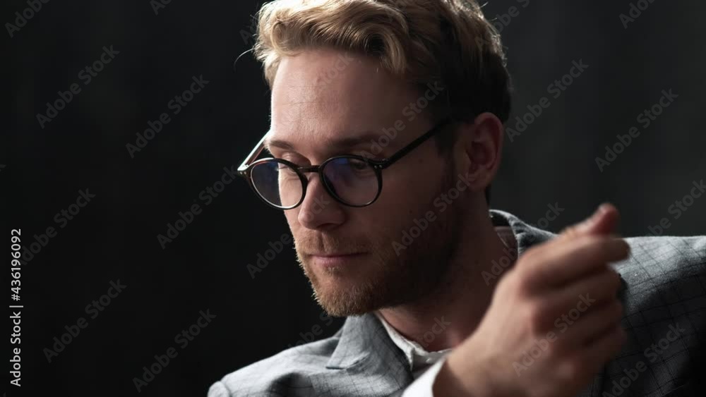 A happy man in a glasses and office suit straightening shirt sleeve and holding glasses in a dark office A happy man in a glasses and office suit straightening shirt sleeve and holding glasses in a dark office