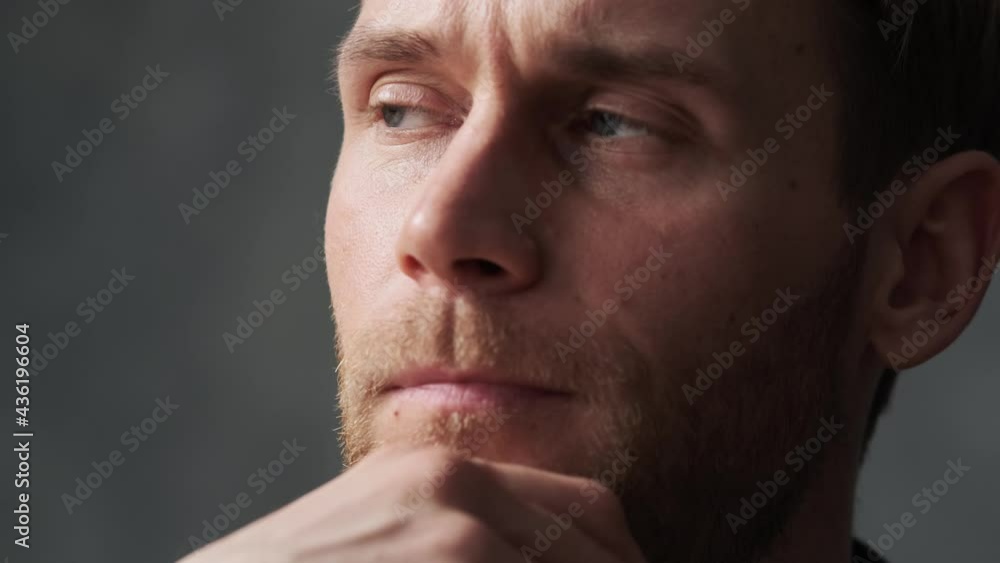 A close-up shot of a pensive man's face rubbing his beard in a gray office A close-up shot of a pensive man's face rubbing his beard in a gray office