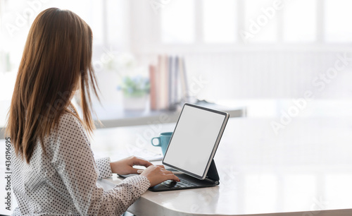 Young woman working on tablet with keyboard while sitting at the table in white office room