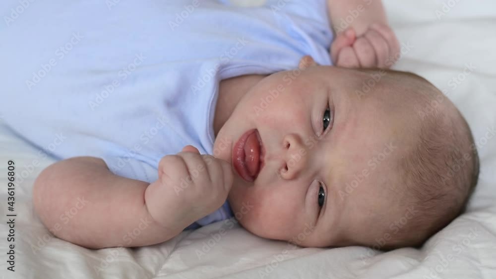 Newborn baby portrait. Close up face infant baby laying on a soft blanket. One month child waking up, opening eyes, yawning and smiling. Hungry little child sucking fingers. Infancy concept. Newborn baby portrait. Close up face infant baby laying on a soft blanket. One month child waking up, opening eyes, yawning and smiling. Hungry little child sucking fingers. Infancy concept.