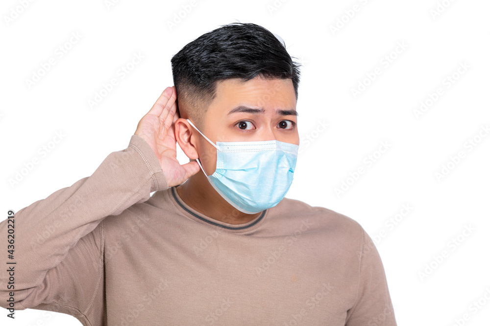 Young man wearing medical mask with hand over ear listening and hearing to rumor or gossip Young man wearing medical mask with hand over ear listening and hearing to rumor or gossip