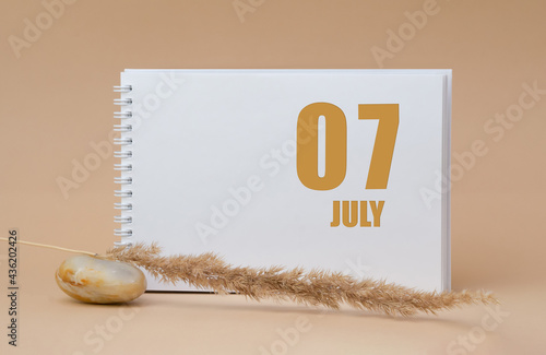 july 07. 07th day of the month, calendar date.White blank sheet of notepad, stones, dry sprig of grass, on beige background.Summer month, day of the year concept photo