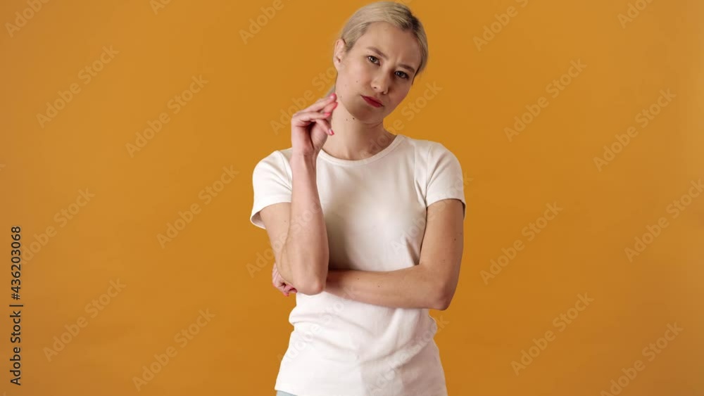A tired blonde asian woman in a t-shirt showing blah blah blah gesture while standing in an orange studio A tired blonde asian woman in a t-shirt showing blah blah blah gesture while standing in an orange studio