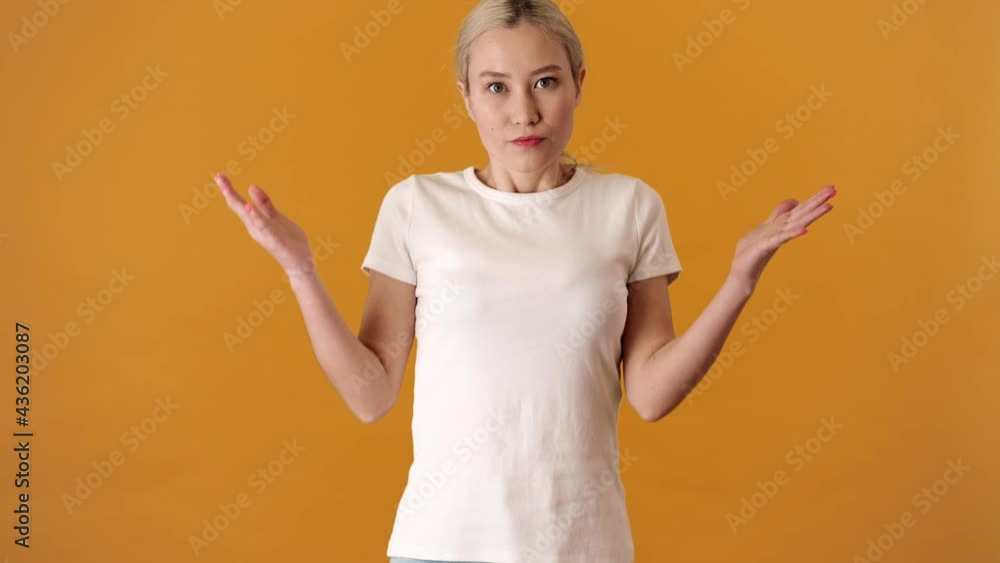 A surprised blonde asian woman in a t-shirt waving her hands and shaking her head negatively while standing in an orange studio A surprised blonde asian woman in a t-shirt waving her hands and shaking her head negatively while standing in an orange studio