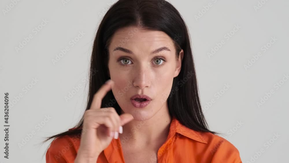 A serious woman is thinking about something while raising her finger up coming up with an idea standing isolated over grey wall in the studio A serious woman is thinking about something while raising her finger up coming up with an idea standing isolated over grey wall in the studio