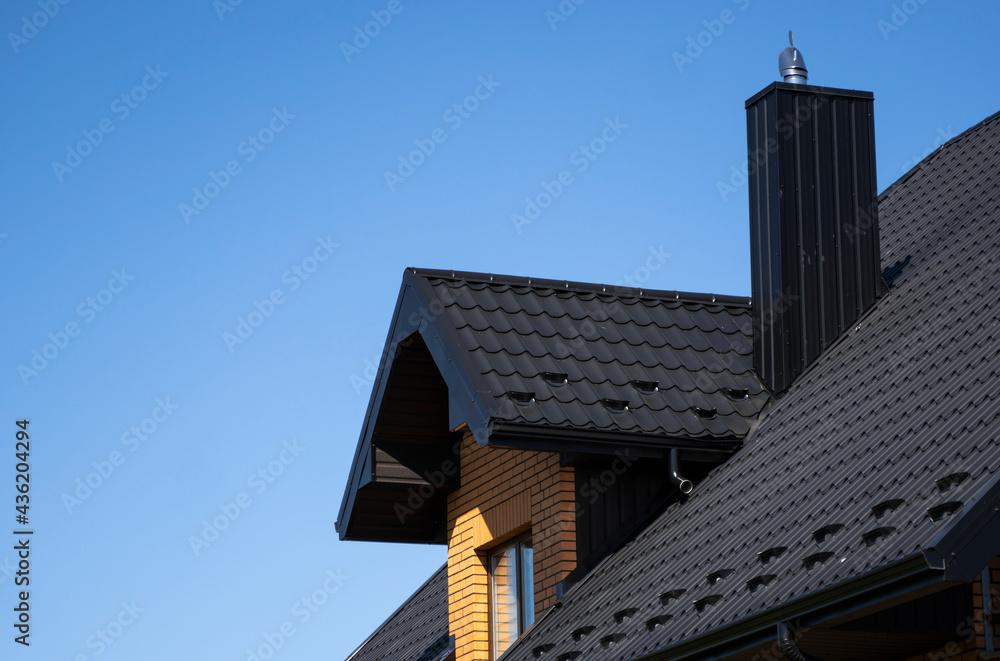 Obraz premium Brown corrugated metal profile roof installed on a modern house. The roof of corrugated sheet. Roofing of metal profile wavy shape. Modern roof made of metal. Metal roofing.