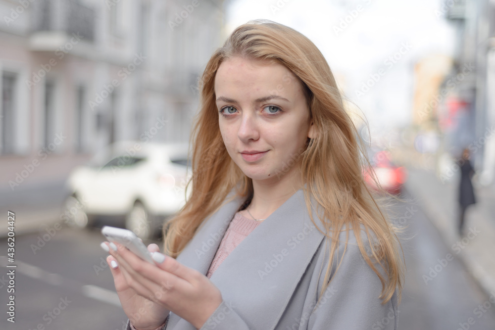 girl with red hair in coat looks something in smartphone on city street