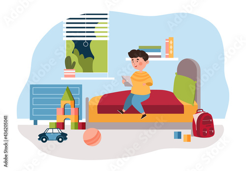 Cute little boy is sitting on bed at home in his bedroom using a digital tablet
