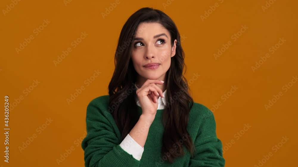 A pensive young woman in a green sweater and shirt thinking about something while standing in an orange studio A pensive young woman in a green sweater and shirt thinking about something while standing in an orange studio