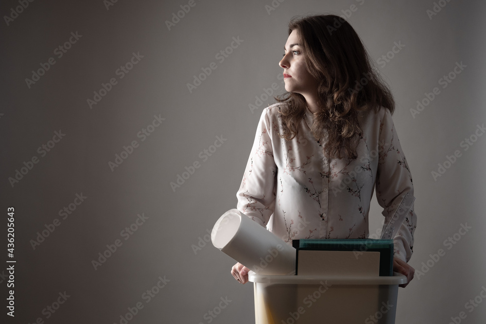 Fired employee on a dark background. The box in the hands symbolizes fired from job. Woman holding box of fired employee. Job loss due to downsizing. Concept - a girl dismissal due to the crisis Fired employee on a dark background. The box in the hands symbolizes fired from job. Woman holding box of fired employee. Job loss due to downsizing. Concept - a girl dismissal due to the crisis