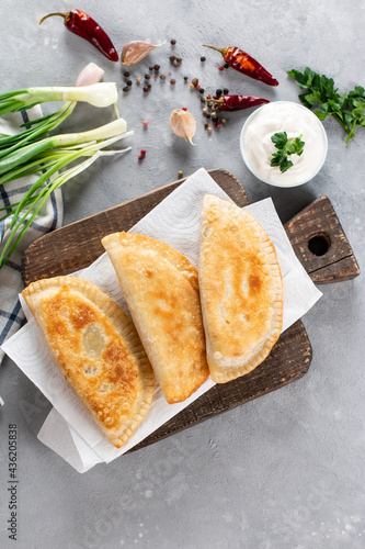 Homemade fried empanadas with pork, chebureks with meat on a wooden board on a gray background. Top view.