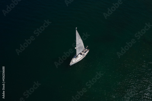 Large white boat with sails on blue water aerial view. Lonely sailboat on the water top view. Sailboat on Lake Garda, Italy. Boat with sails, blue water with high altitude.