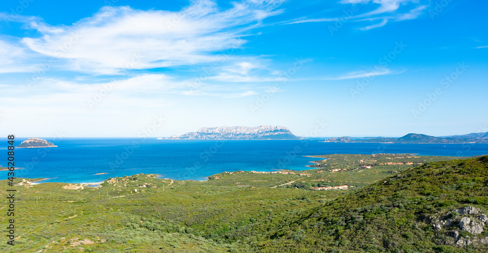 View from above, stunning aerial view of a green coastline bathed by a turquoise Mediterranean sea with Tavolara Island in the distance. Sardinia, Italy.
