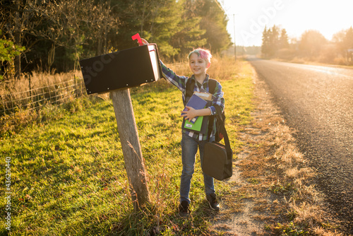 Boy standing at mailbox on roadside at sunset photo