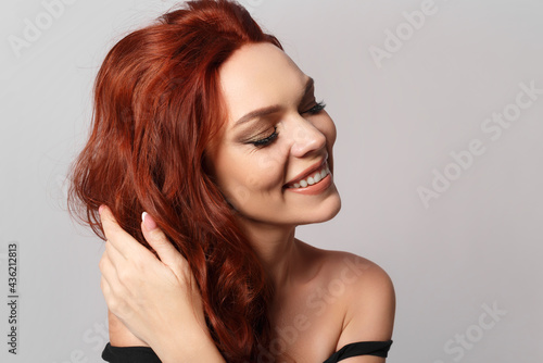 Beauty portrait of a red-haired happy beautiful woman on gray.