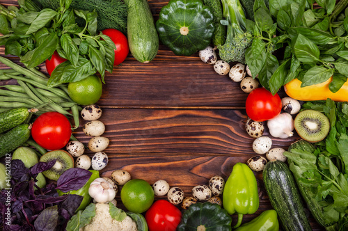 Frame of assorted fresh vegetables. Still Life. Ripe vegetables. High angle of wooden cutting board surrounded by fresh herbs and assortment of raw vegetables on rustic wood table. Empty vintage frame