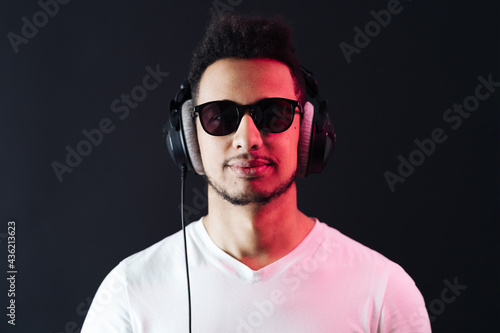 Smile Young African American man portrait wearing headphones and enjoy music over black Background. Red light reflection on face.