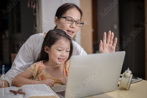 Asian woman teaching her duagther with laptop and smartphone study online concept. photo