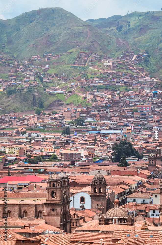 Aerial view of rooftops in Cusco city with the valley surrounded by green fields. Houses and churches from a fair away point. Peru, South America