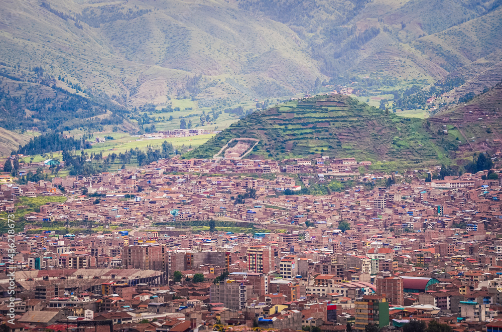 Aerial view of rooftops in Cusco city with the valley surrounded by green fields and hills in the bottom. Houses and churches from a fair away point. Peru, South America