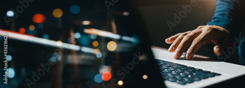 young man hand working on a laptop, bokeh blurred at night For text copy space, image size horizontal photo