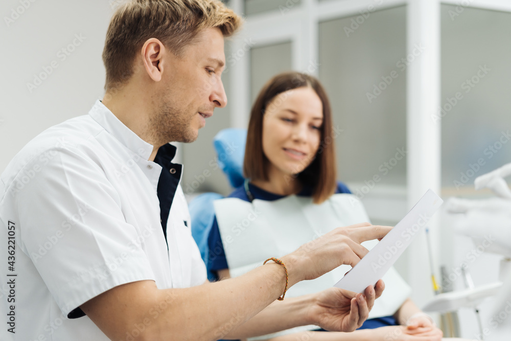 Fototapeta premium Male Professional Dentist With Gloves And Mask Holding papers photo And Show What The Treatment Will Look Like Of The Patient's Teeth. Discussion Of The Treatment Plan And Healthy Smile