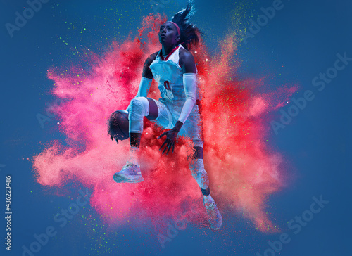 One young woman sportsman basketball player in explosion of colored neon powder isolated on dark blue background