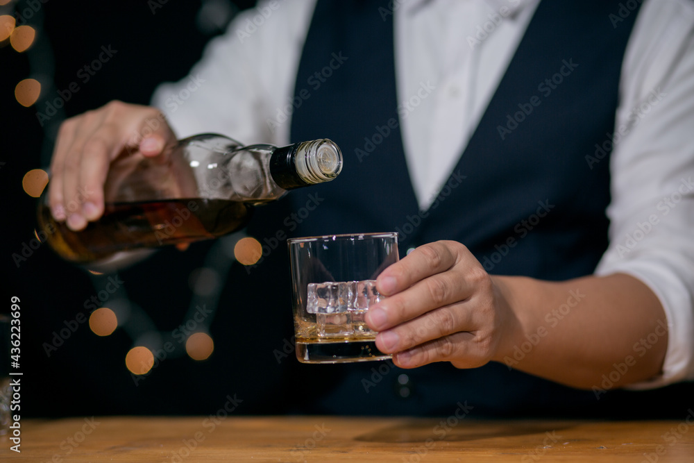 Waitress man standing pours whiskey into a glass celebrate whiskey on a friendly party in restaurant