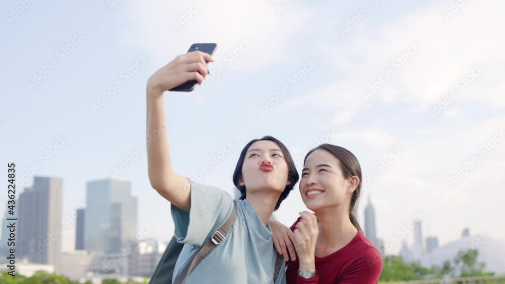 Two Beautiful Asian teenage woman using smartphone to take selfies. Tourists happy take pictures from mobile phones while traveling in city. Freedom to travel with safety. Concept travel insurance Two Beautiful Asian teenage woman using smartphone to take selfies. Tourists happy take pictures from mobile phones while traveling in city. Freedom to travel with safety. Concept travel insurance