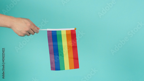 Hand is holding a rainbow flag on mint green or tiffany blue background.