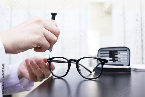 Eyeglass repair. Close-up of the hand of a master who uses a screwdriver to tighten a screw in a spectacle frame. Optics salon and repair shop
