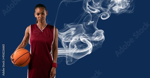 Composition of mixed race female basketball player holding ball with smoke and copy space