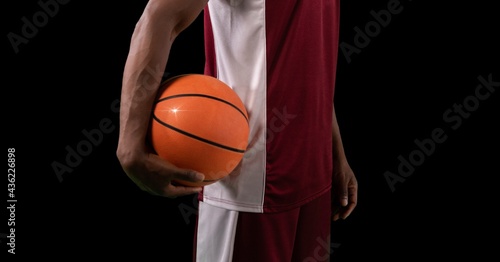 Composition of midsection of male basketball player with ball and copy space on black background © vectorfusionart