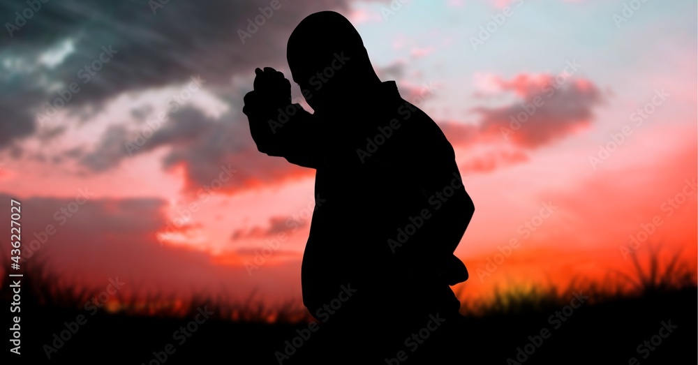 Composition of silhouette of male martial artist over sky with sun setting