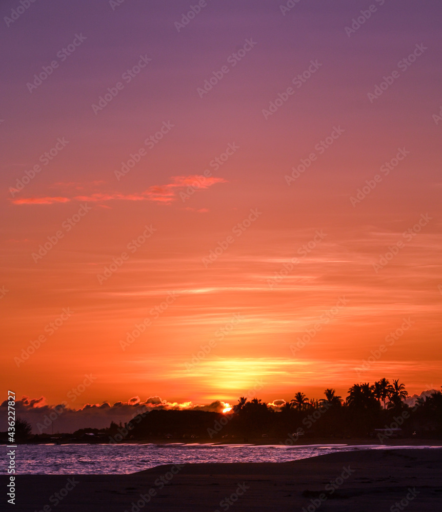 The beach at sunset with golden orange skies and clouds as the sun dips into the ocean