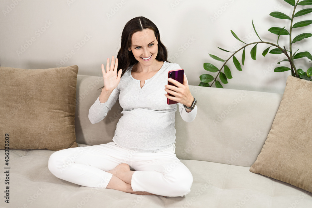 pregnant woman communicates on smartphone while sitting on couch, video link pregnant woman communicates on smartphone while sitting on couch, video link