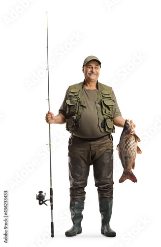 Full length portrait of a happy fisherman in a uniform holding a big carp fish and a fishing rod