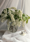 Branches of white bird cherry in a transparent vase next to a figurine of birds. 