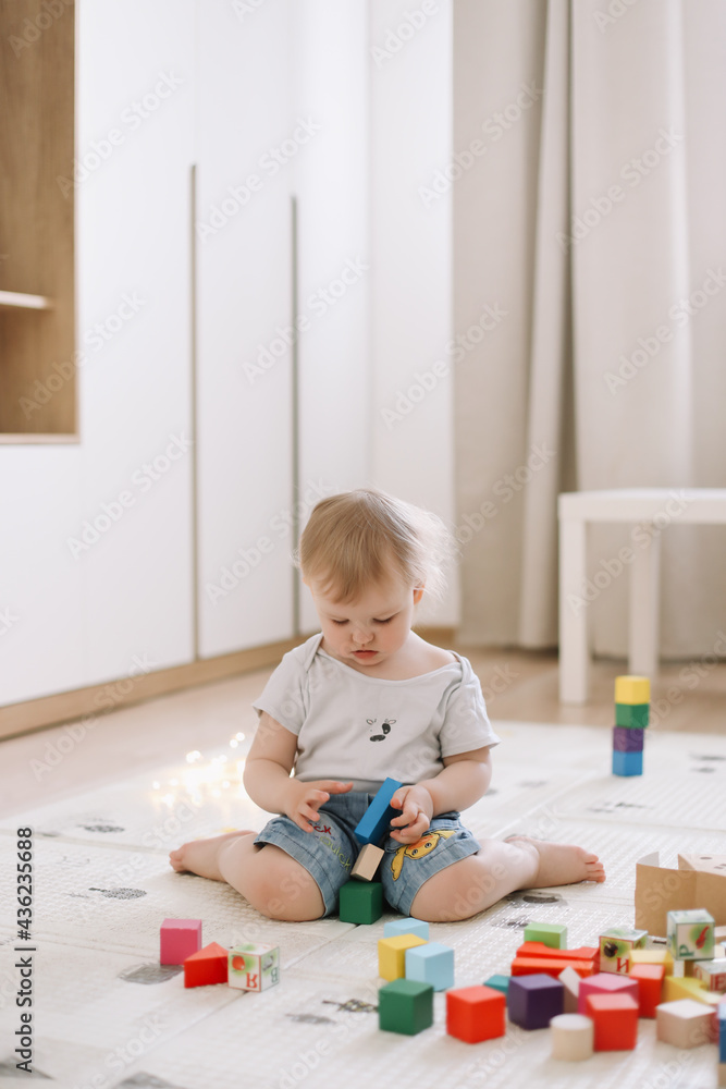 Little girl playing with colorful wooden brickes on the floor in the kids room Little girl playing with colorful wooden brickes on the floor in the kids room