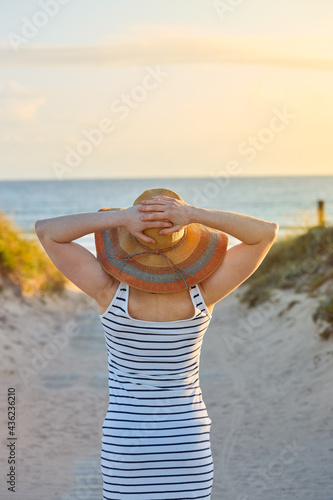Close-up of a girl on her back with straw hat on a path to the beach.