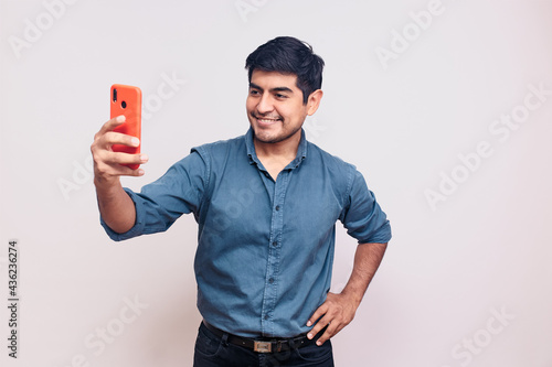 Hombre joven y feliz tomando una foto selfie mientras sonrie. Modelo aislado en fondo blanco camisa azul photo