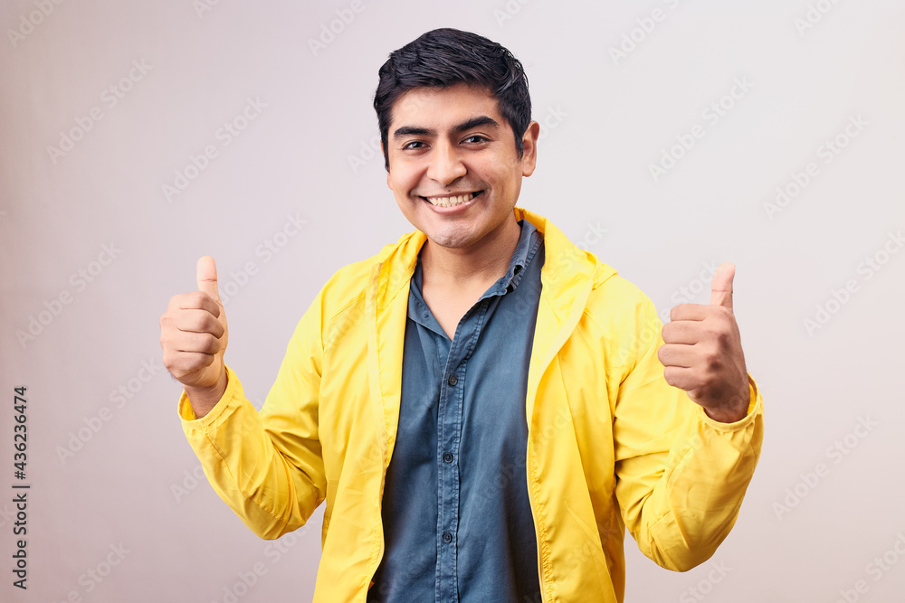 Hombre joven y feliz levanta pulgares. Modelo aislado en fondo blanco con casaca amarilla Hombre joven y feliz levanta pulgares. Modelo aislado en fondo blanco con casaca amarilla