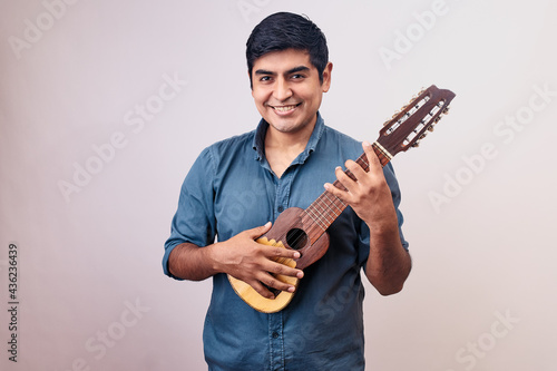 Hombre joven y feliz sonriendo en primer plano con un charango. Modelo aislado en fondo blanco con camisa azul photo