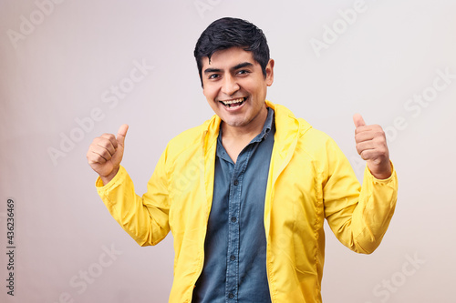 Hombre joven y feliz levanta pulgares. Modelo aislado en fondo blanco con casaca amarilla photo