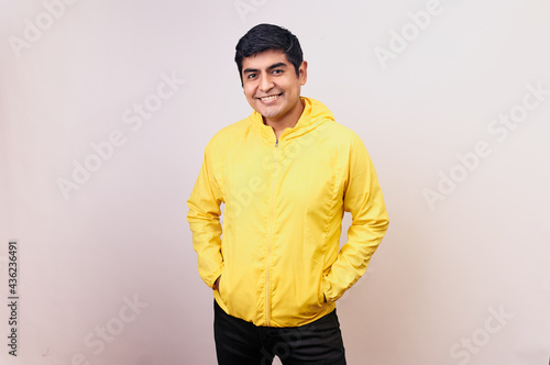 Hombre joven y feliz mira directo a la cámara. Modelo aislado en fondo blanco con casaca amarilla