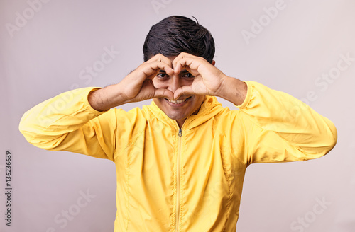 Hombre joven y feliz hace gestos de amor con sus manos. Modelo aislado en fondo blanco con casaca amarilla photo